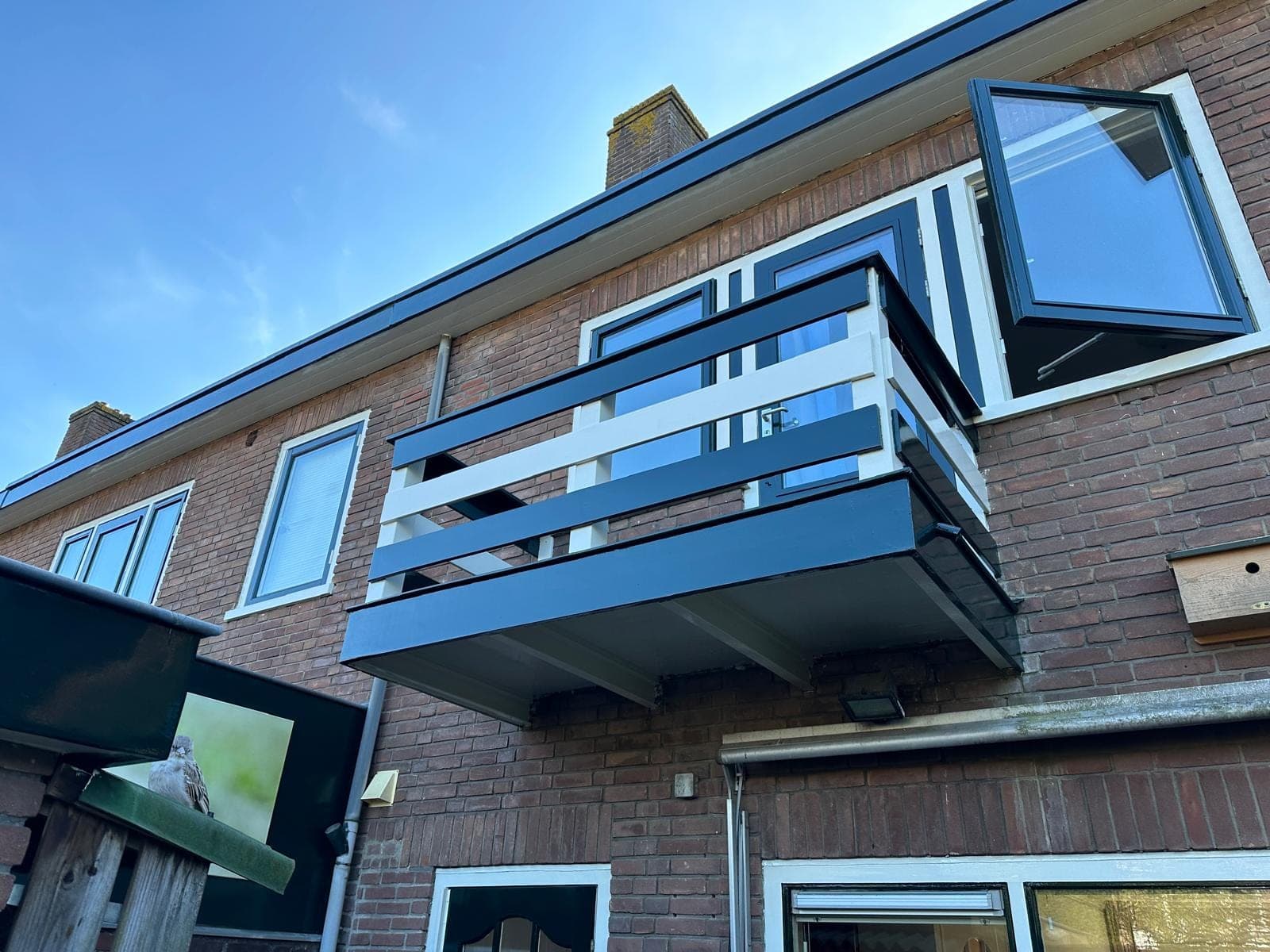 Opengedraaid raam naast het balkon, met witte kozijnen en donkergroene dakrand