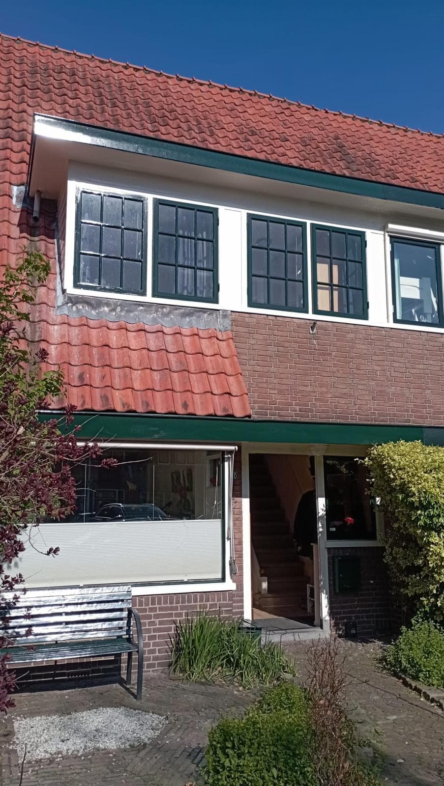 Voorgevel van de jaren-30 woning met witte bovenramen, donkergroene kozijnen en rode dakpannen