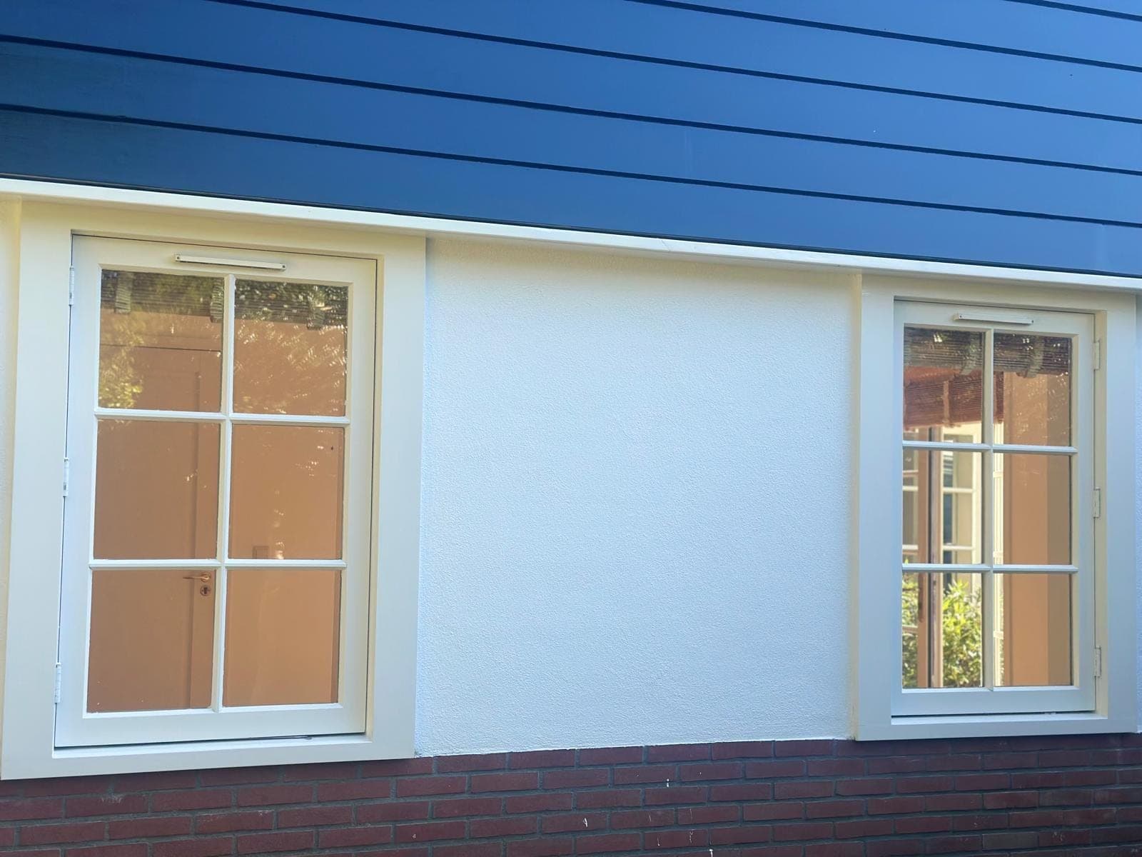 Diepblauw potdekselwerk boven een witte gevel met twee crèmewitte kozijnen met roedes