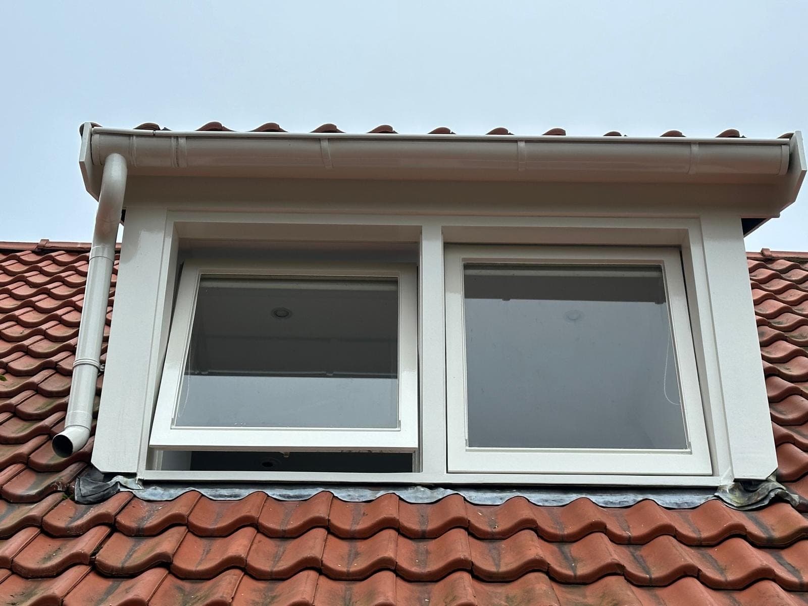 Dakkapel met twee witte kozijnen, witte goot en nieuw lood in een rood pannendak