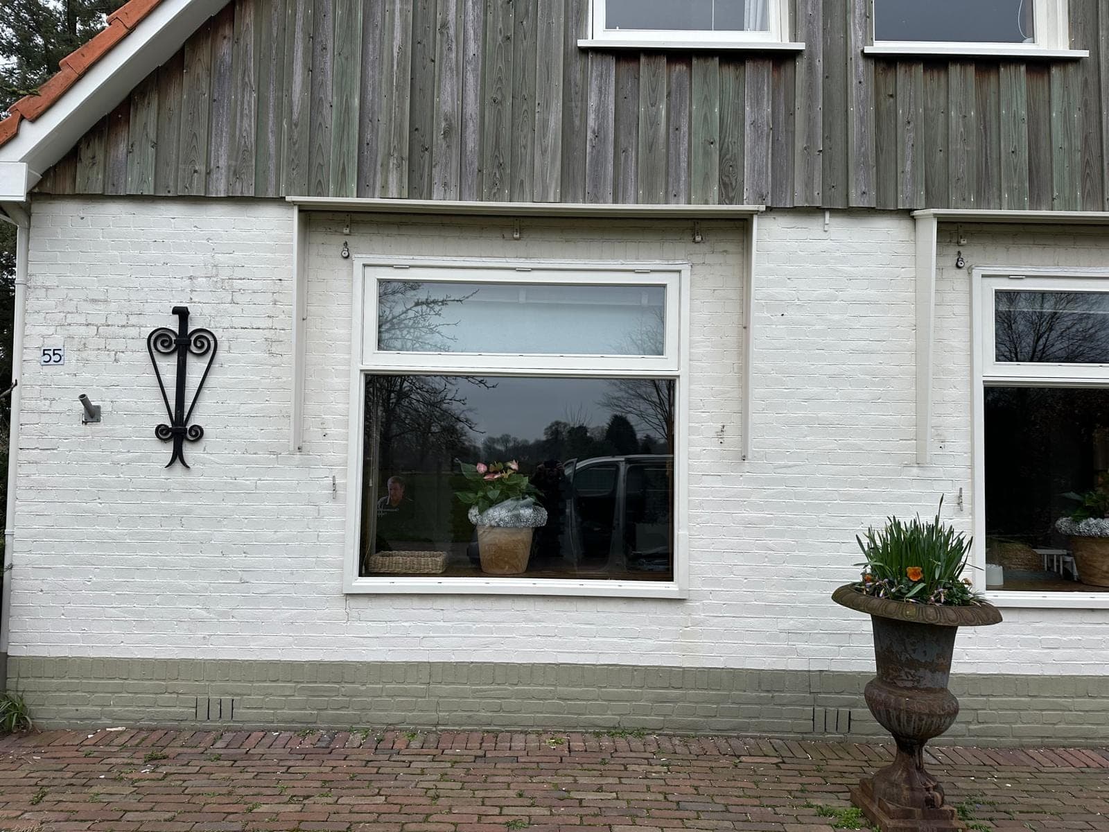 Wit kozijn met bovenlicht onder de houten topgevel, met een smeedijzeren muuranker