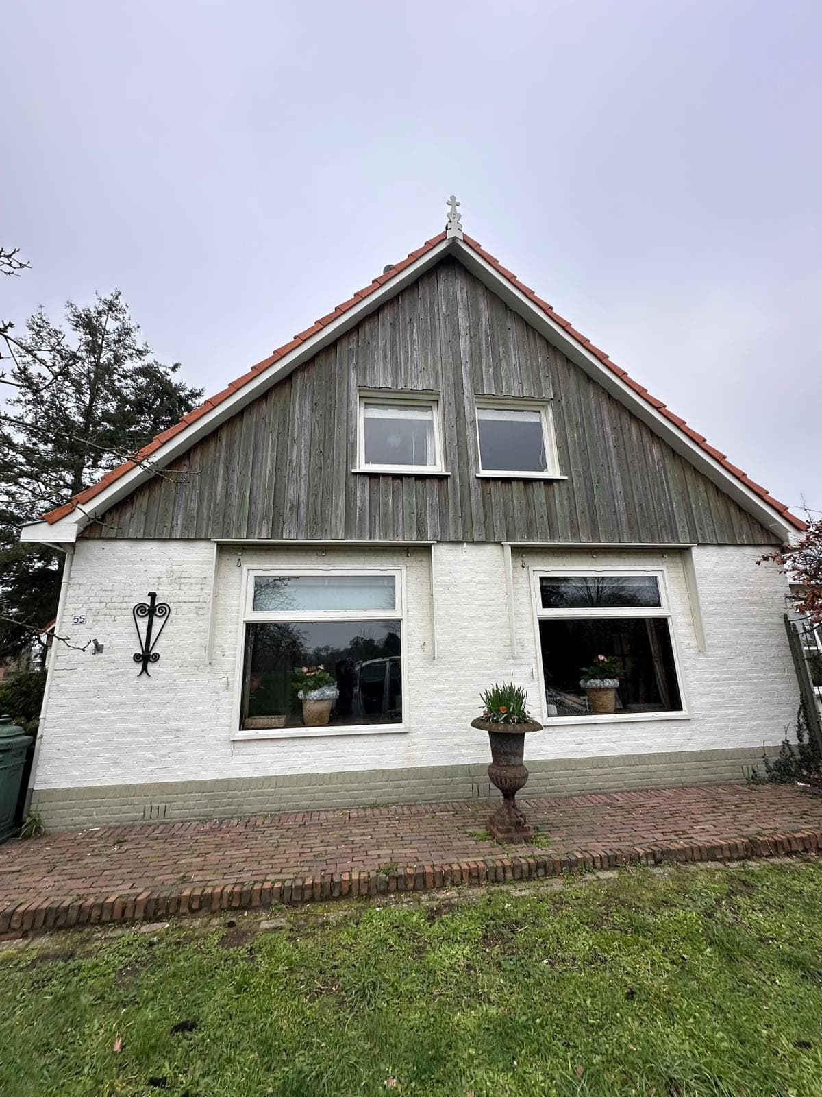 Witte boerderijwoning met vergrijsde houten topgevel en witgeschilderde kozijnen