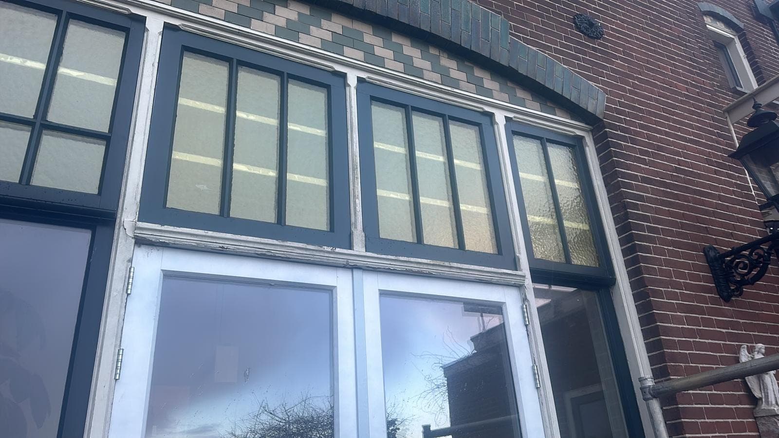 Donkergroen boogkozijn met glas-in-lood bovenlichten en witte deuren onder siermetselwerk