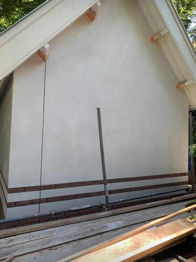 De gestuukte topgevel in gebroken wit met de rode bakstenen plint in het zicht