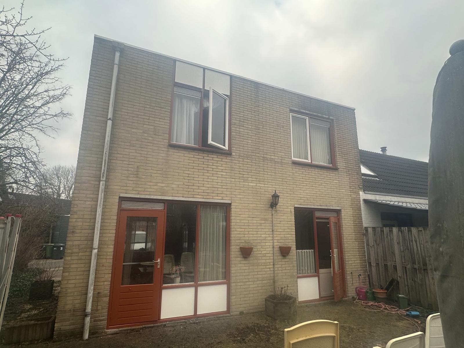 Achtergevel van een jaren-80 woning in gele baksteen met roodbruine kozijnen en deuren