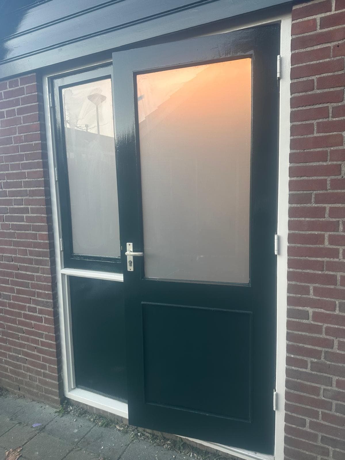 Donkergroene dubbele deur met matglas in een wit kozijn in rode baksteen