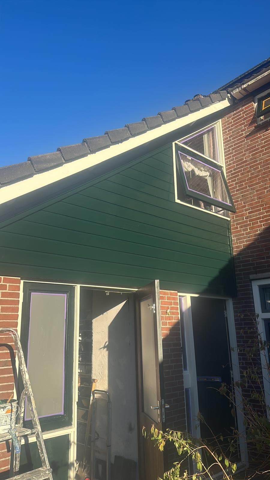 Groene houten topgevel tijdens het werk, met ladder en openstaande deuren