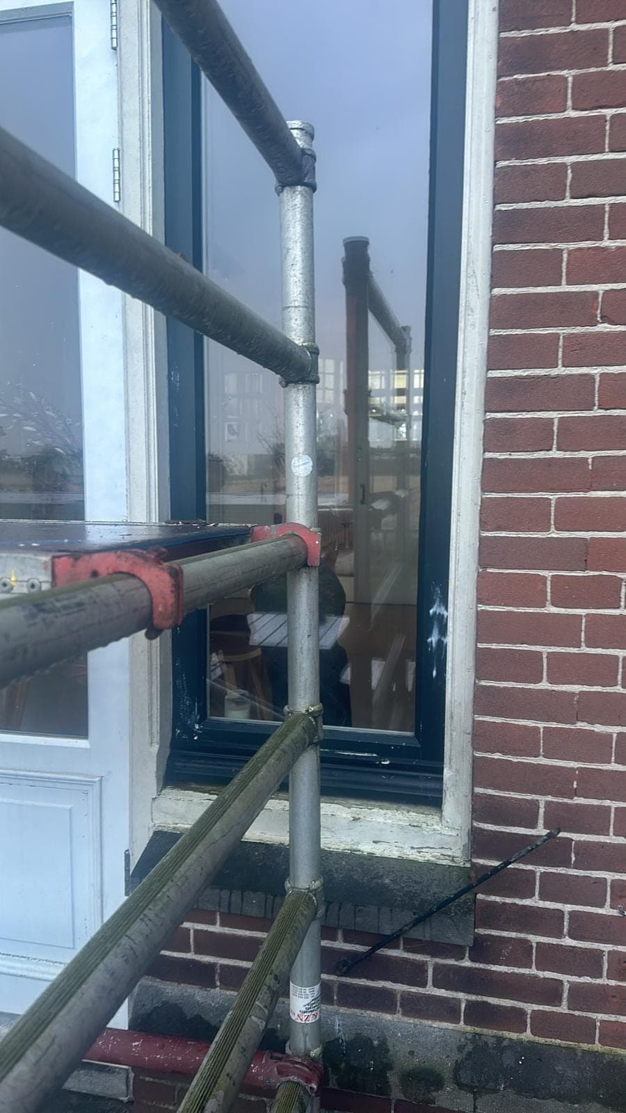 Donkergroen kozijn met witte deur achter de steigerbuizen