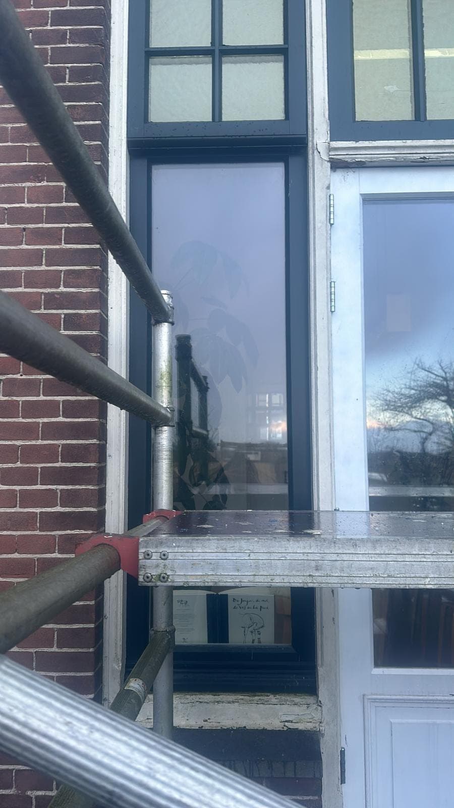 Steiger voor een hoog kozijn met glas-in-lood bovenlicht aan een bakstenen gevel