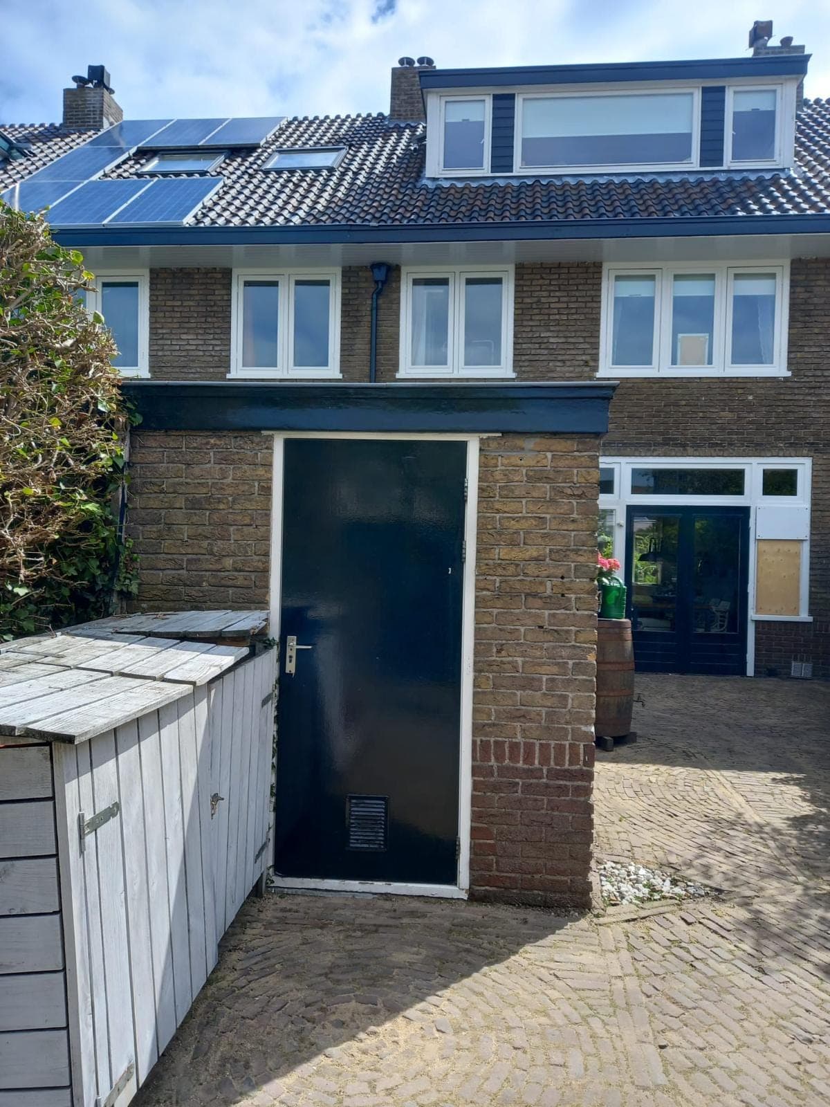 Donkergroene bergingdeur in een gemetselde aanbouw met de achtergevel en dakkapel erachter