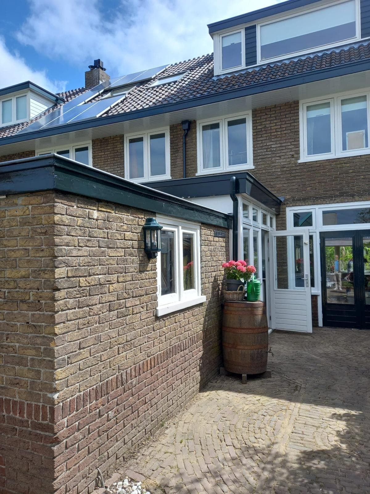 Achtertuin met gemetselde aanbouw, witte kozijnen en donkergroene tuindeuren