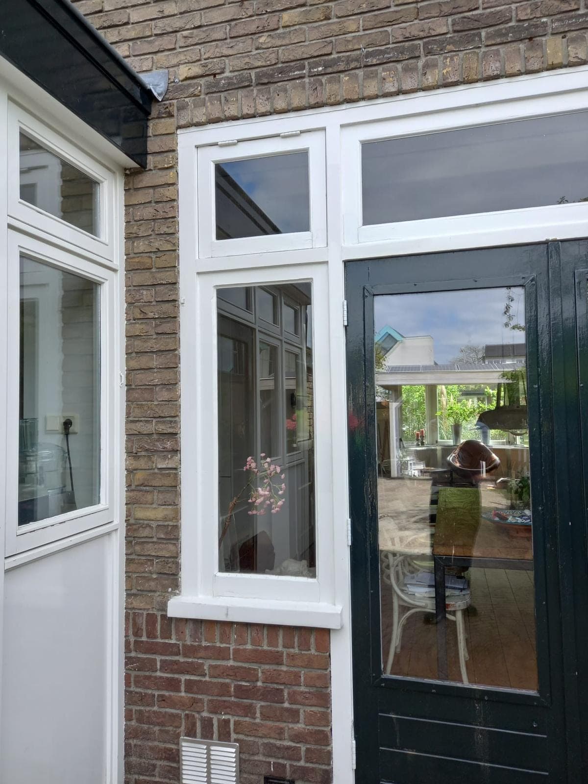 Donkergroene tuindeur met glas naast witte kozijnen en bovenlichten in gele baksteen