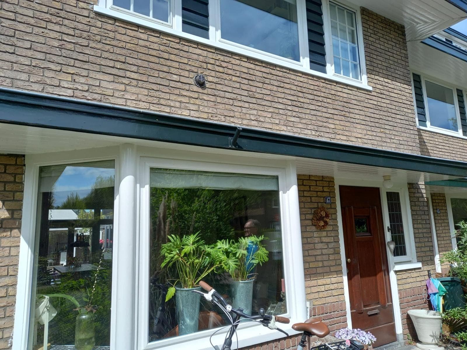 Witte erker en voordeur van een jaren-30 woning onder een donkergroene luifelrand