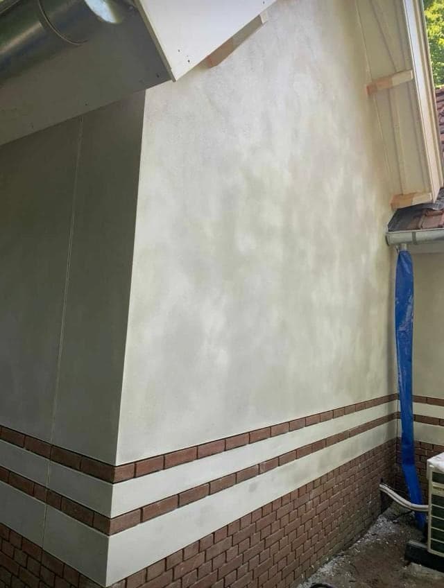 Hoek van de gestuukte gevel met de rode plint en sierband