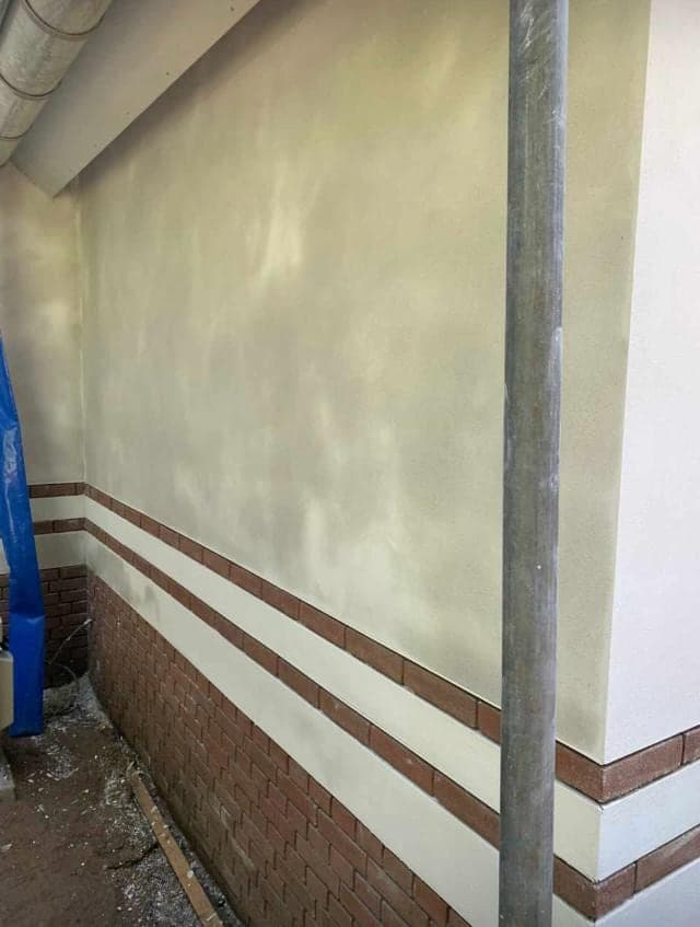 Detail van de overgang tussen stucwerk en de rode bakstenen plint