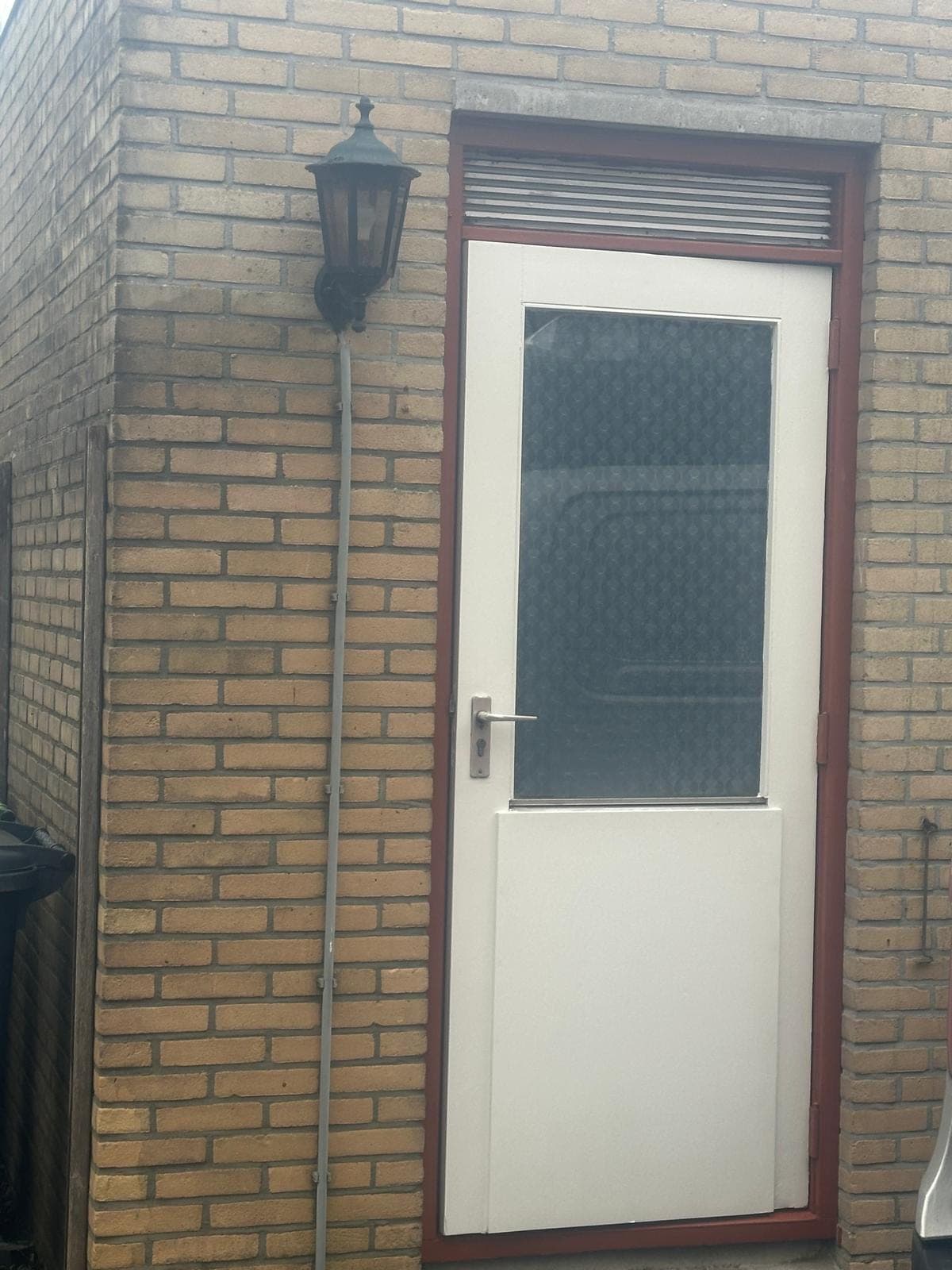 Witte bergingdeur met glas in een roodbruin kozijn met ventilatierooster