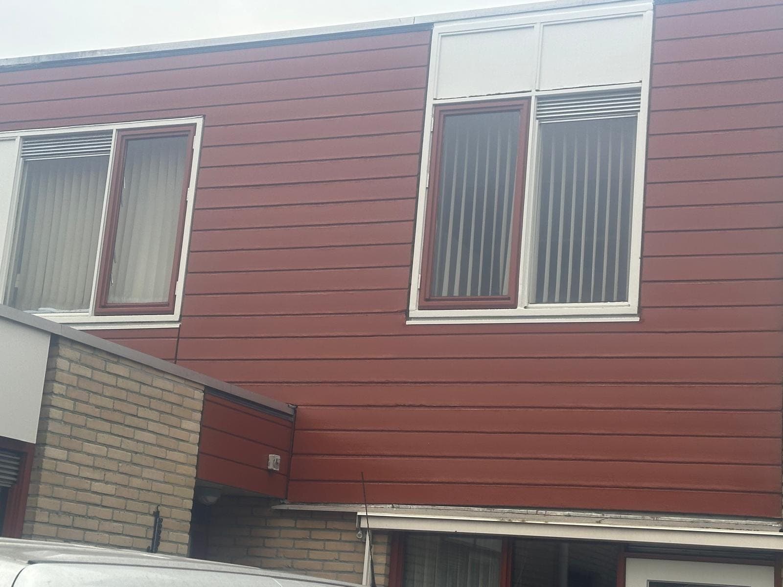 Roodbruine houten gevelbekleding met kozijnen en witte panelen op de verdieping