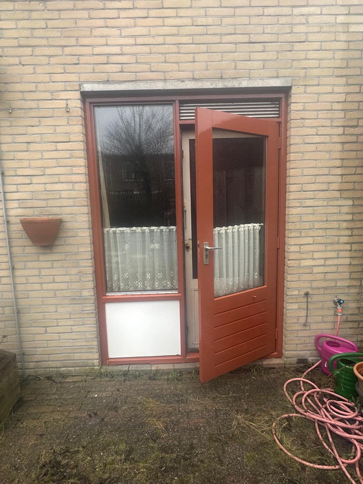 Openstaande roodbruine tuindeur met ventilatierooster en wit paneel