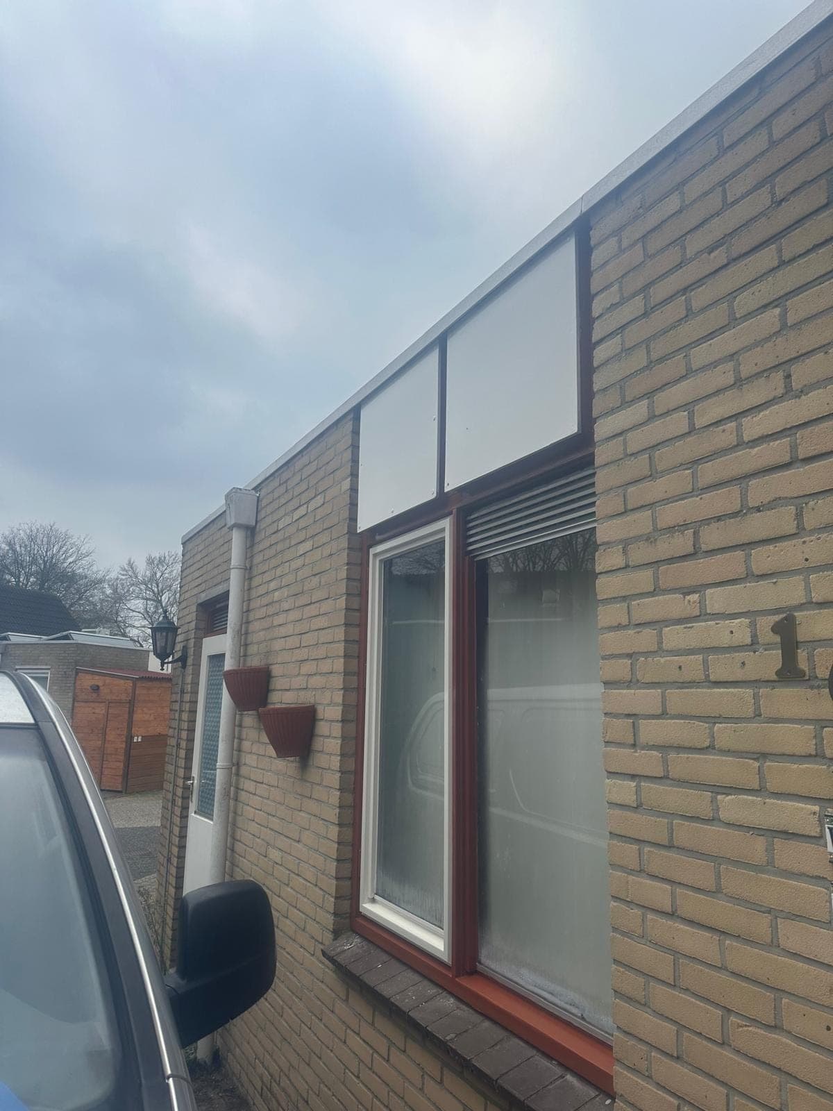 Zijgevel met roodbruin kozijn, ventilatierooster en witte panelen erboven
