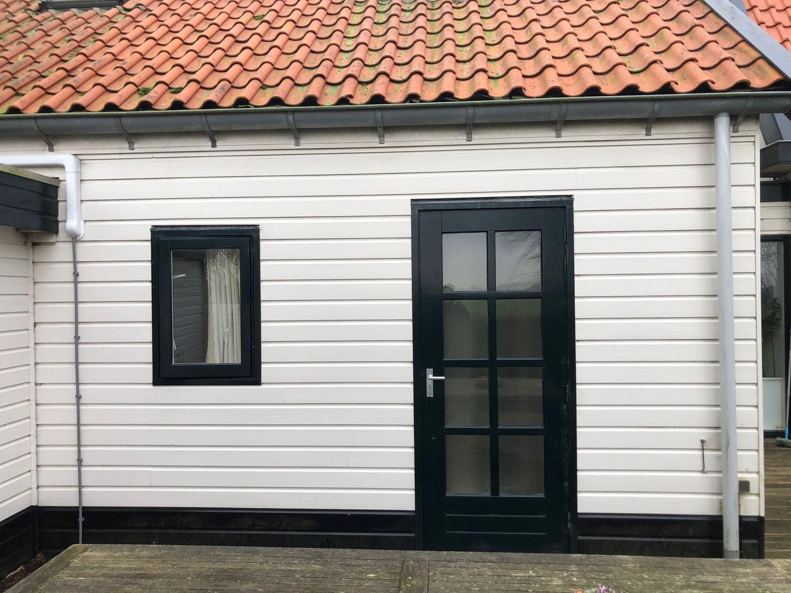 Zwarte achterdeur met roedes in een witte houten gevel