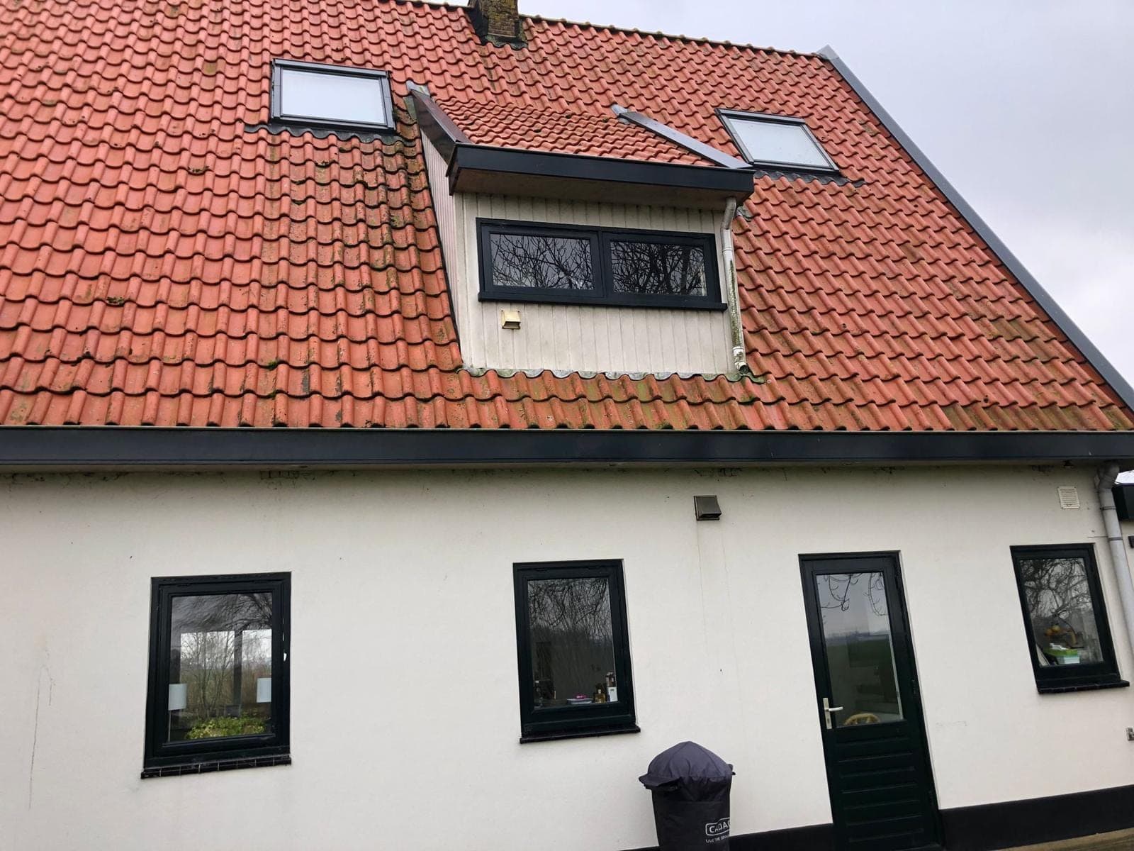Witte gevel met zwarte kozijnen, zwarte deur en een dakkapel in een rood pannendak