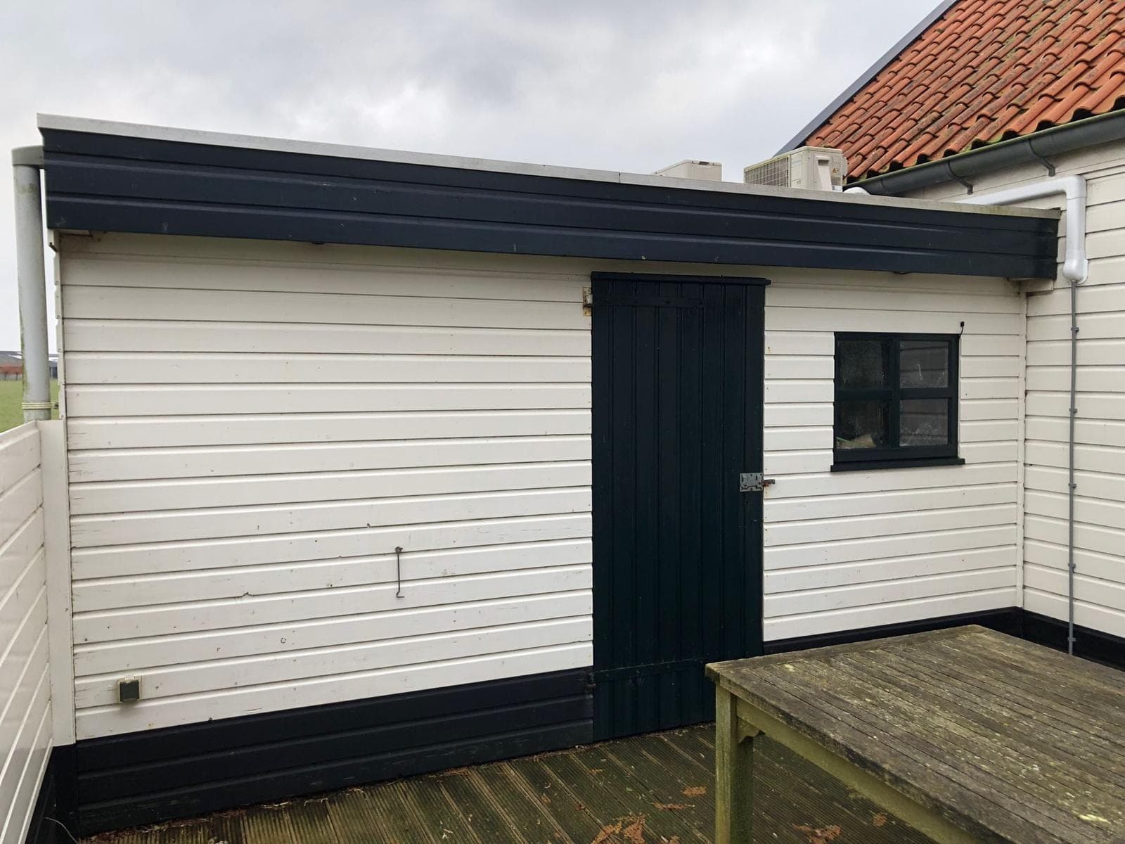 Witte houten berging met zwarte deur en zwart kozijn op een houten vlonder