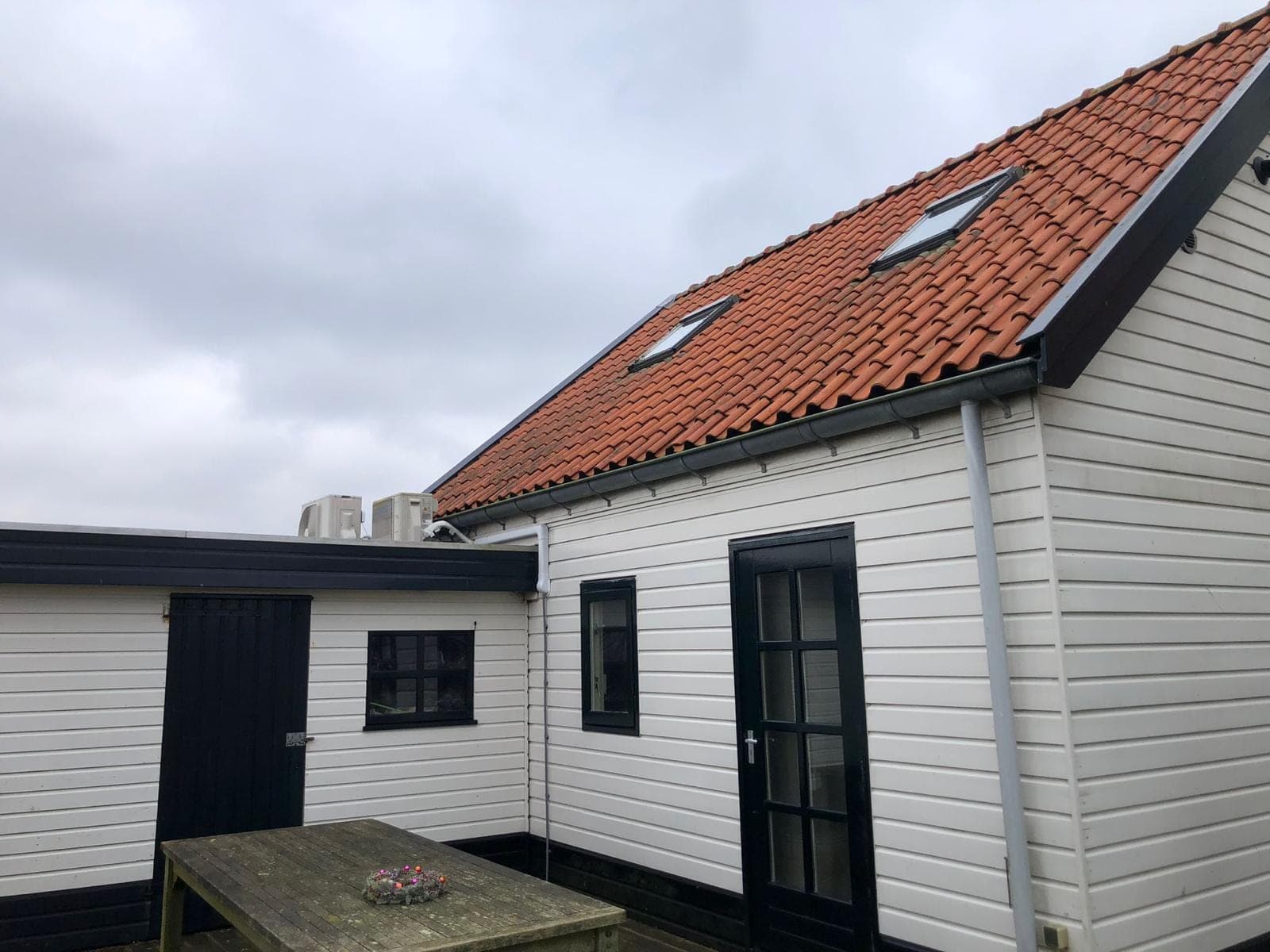 Houten aanbouw in wit potdekselwerk met zwarte deur en zwarte kozijnen
