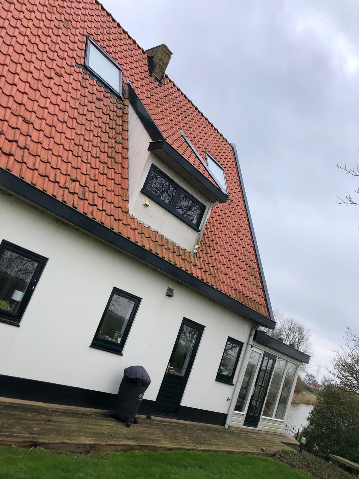 Zijgevel van de witte woning met zwarte kozijnen, een houten vlonder en het water erachter
