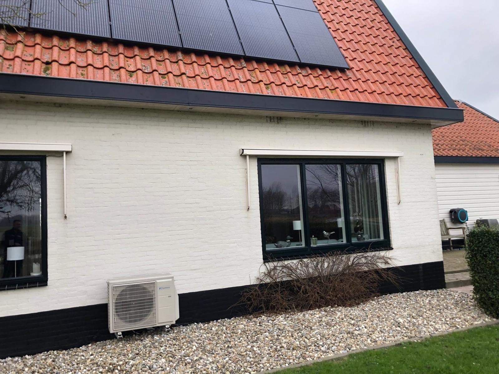 Witte gevel met zwart kozijn en zwarte plint onder een pannendak met zonnepanelen